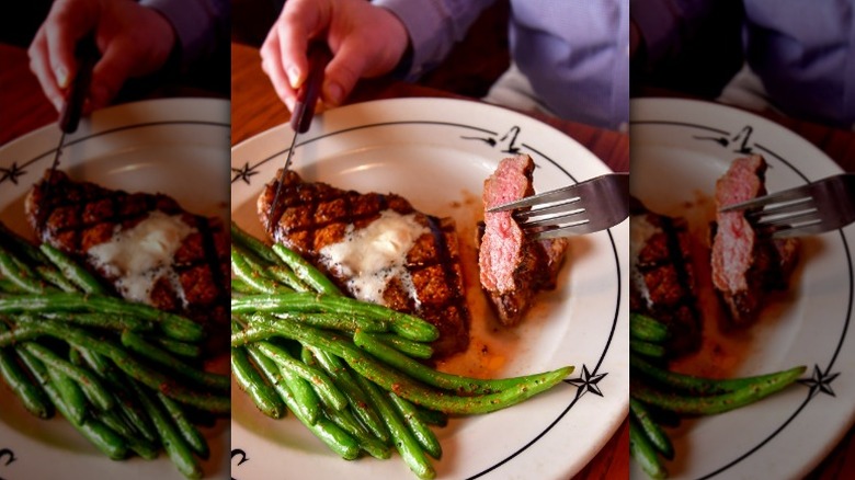 A steak topped with butter served with seasoned green beans from Saltgrass Steak House.