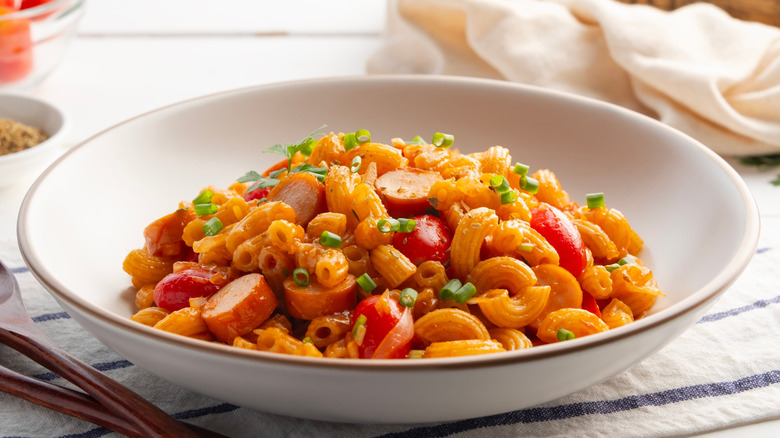 A bowl of macaroni, hot dogs, and tomatoes