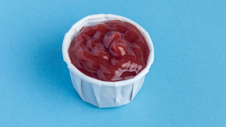 A small paper cup of ketchup on a blue background