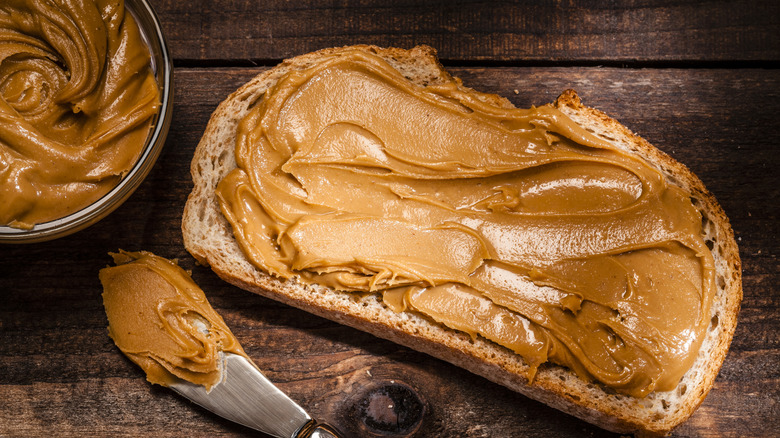 Peanut butter being spread over a slice of bread