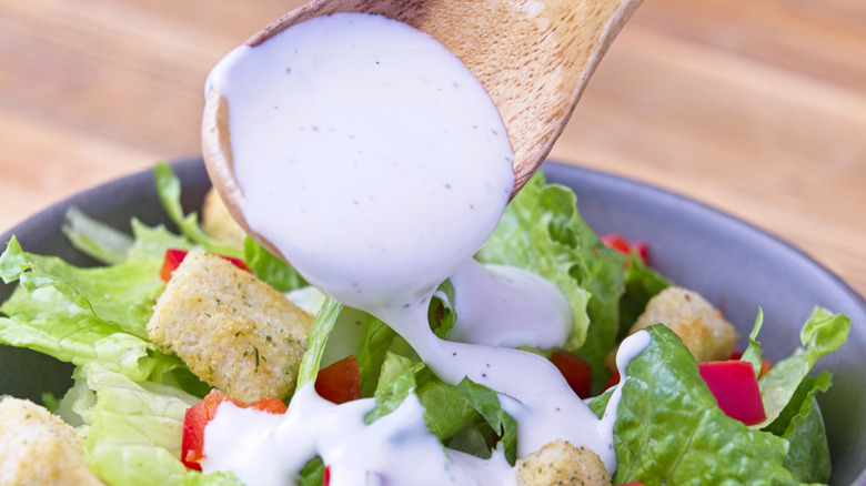 Close-up of a wooden spoon ladling ranch dressing over a salad