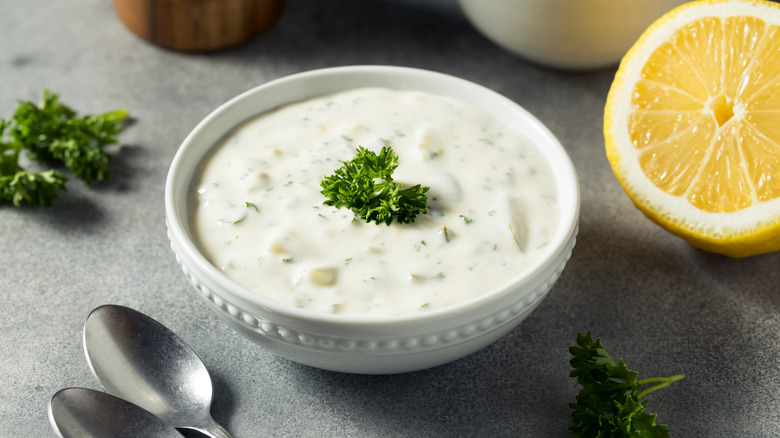 A bowl of tartar sauce next to a lemon and spoons