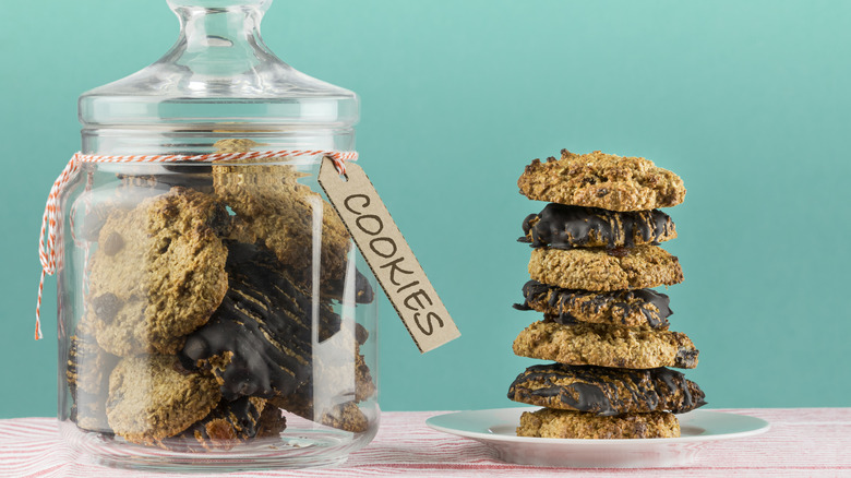 A glass jar of cookies rests beside a plate of stacked cookies