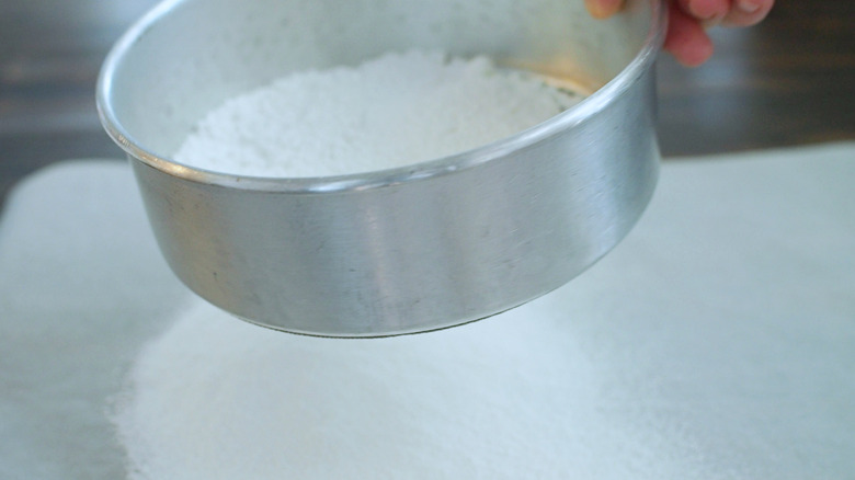 Flour is being sifted through a metal rimed flour sifter