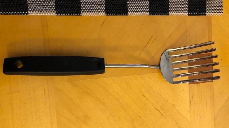A Foley fork with a black handle rests on a wooden table