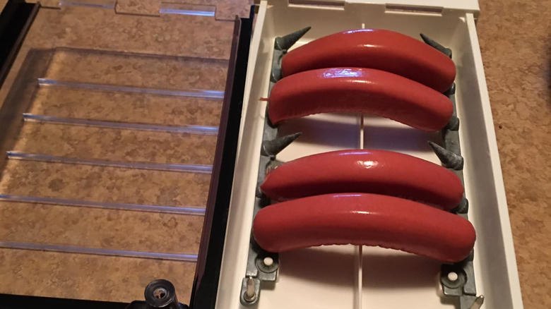 A hot dog zapper rests on a table with four hotdogs on the electrodes inside