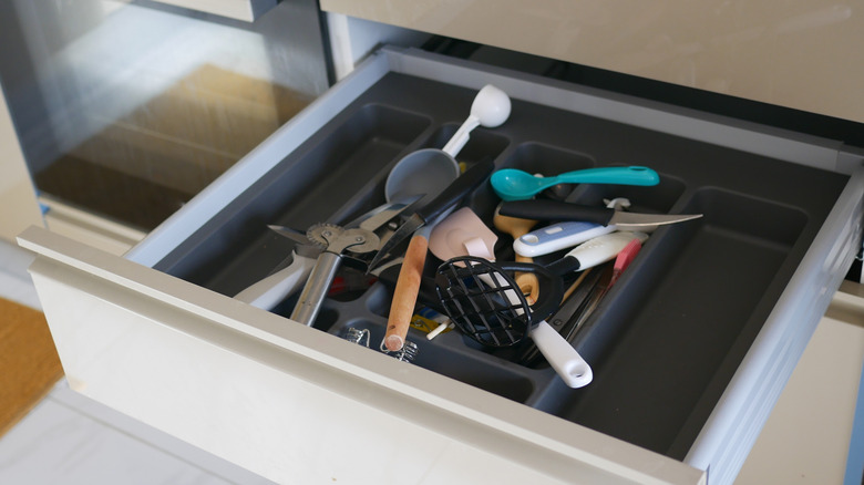 A kitchen drawer is open, filled with a jumble of kitchen utensils