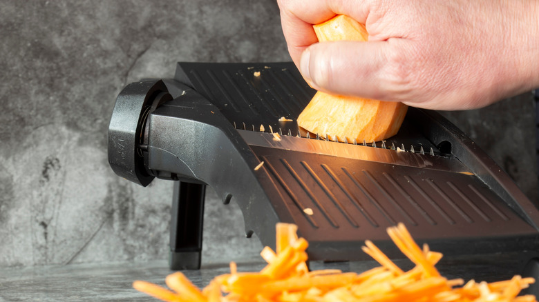 A sweet potato is being sliced on a mandoline slicer