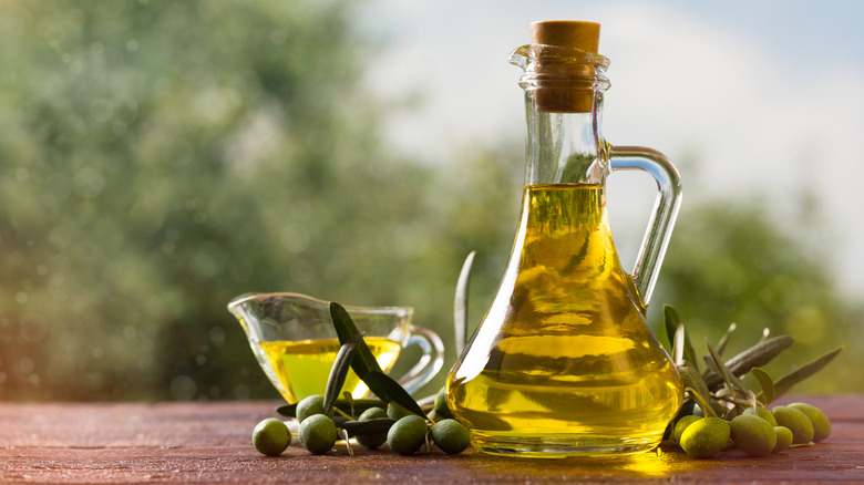 Glass bottle of olive oil and some olives on a wooden table outdoors