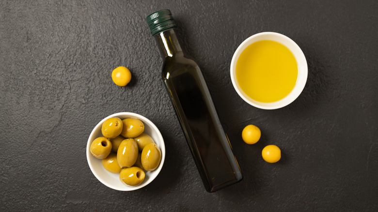 Olives and olive oil in white bowl with bottle of olive oil on dark background