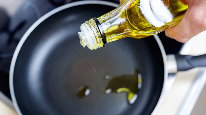 Bottle of oil being poured into a pan on the stove