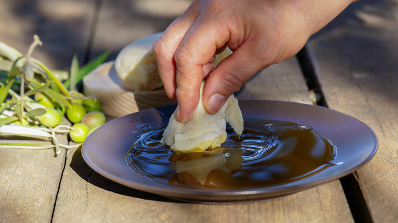 Hand dipping a piece of fresh bread into a shallow plate of extra virgin olive oil