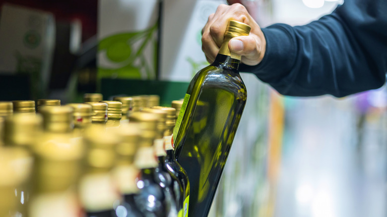 Person's hand selecting a bottle of olive oil from a grocery store shelf