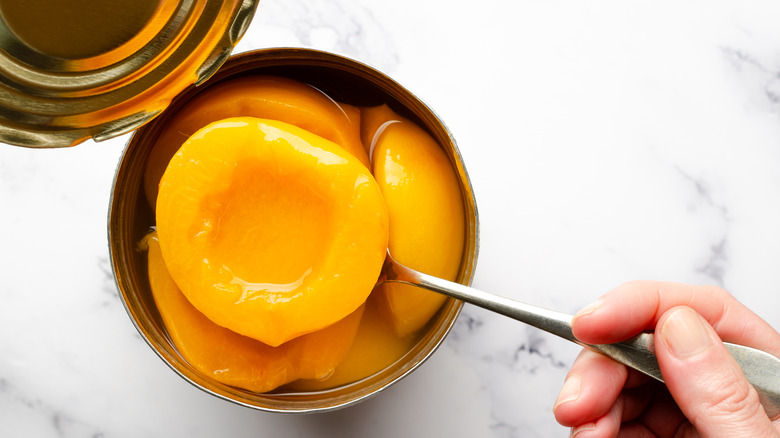 Hand holding a spoon and lifting peach halves out of an open can