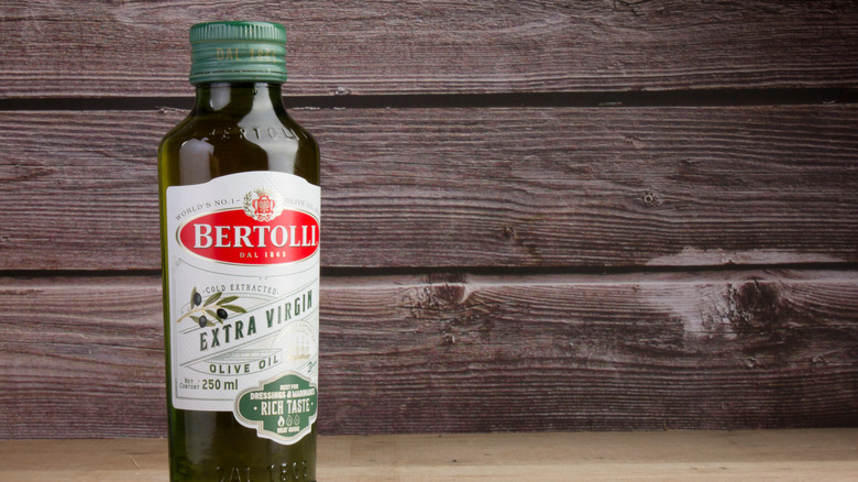 a single bottle of bertolli olive oil in front of a wooden background