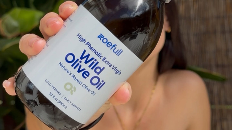 woman holding a bottle of zoefull wild olive oil, blocking her face