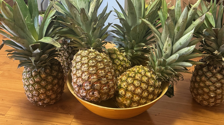 Several pineapples in a large bowl and on a wooden table