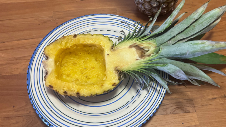 A half pineapple sliced vertically and hollowed out to form a bowl on a blue and white plate