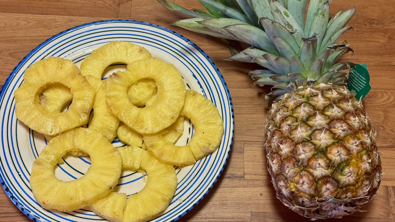 Rings of sliced pineapple on a blue and white plate next to a whole pineapple on a wooden table