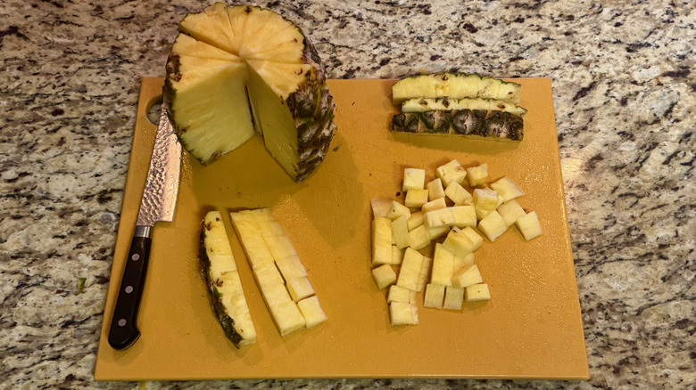 A yellow cutting board with a pineapple standing upright cut into multiple wedges