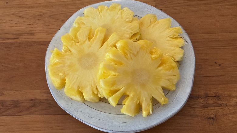 Thick rings of pineapple with notched edges like flowers on a white ceramic plate