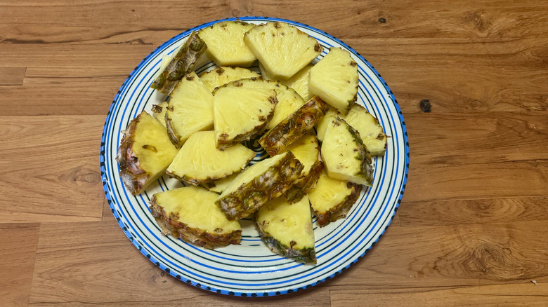 Small wedges of pineapple with the rind attached to one end on a blue and white plate