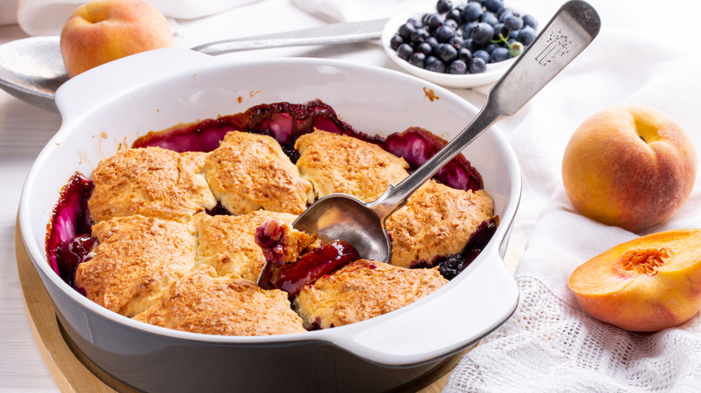 Freshly baked peach and blueberry cobbler surrounded by fruit