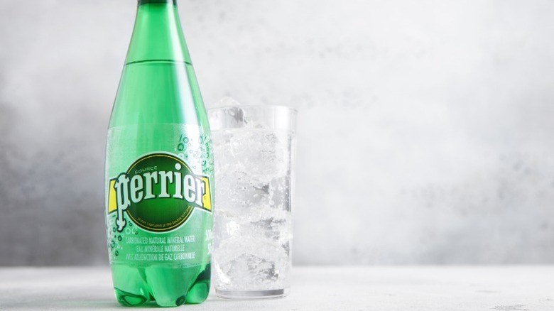 A bottle of Perrier water next to a glass.