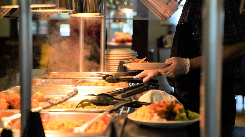 a person's gloved hands reaching for tongs at a buffet full of food at Furr's