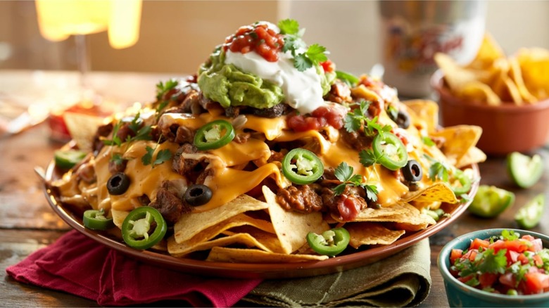 Loaded nachos piled high with melted cheese, jalapeños, black olives, salsa, sour cream, and guacamole, served on a party platter.