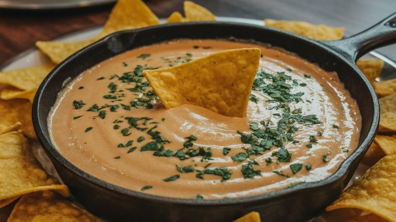A small cast iron skillet of queso cheese dip surrounded by tortilla chips for a delicious Tex-Mex snack