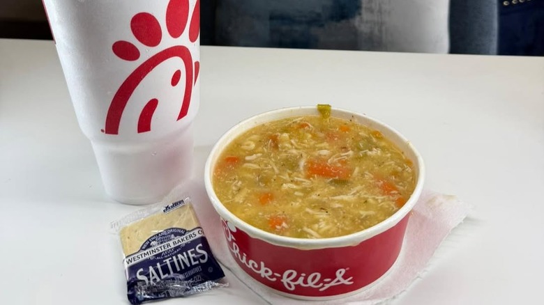 A large bowl of Chick-fil-A's Chicken Noodle Soup with saltines and a large drink.
