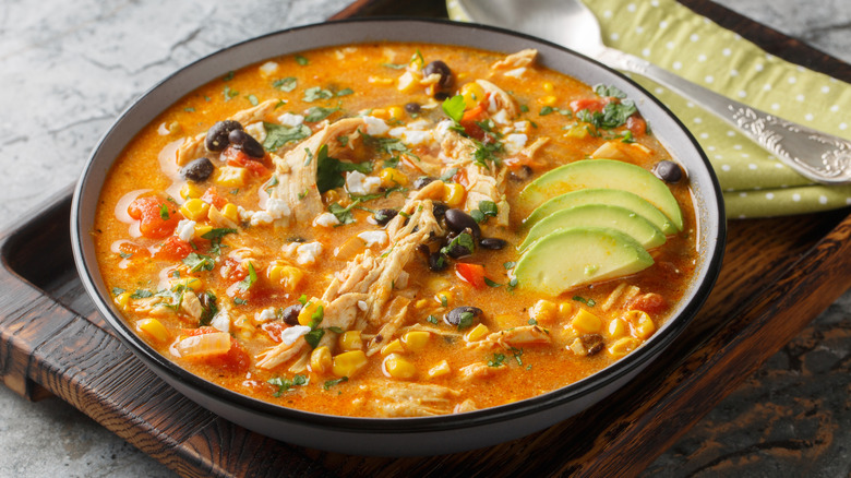 A bowl of Chicken Tortilla Soup with avocado sitting on a cutting board.