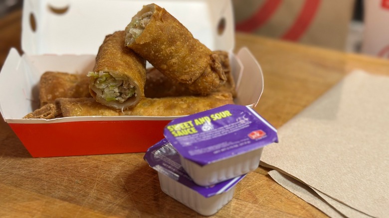 A box of three Jack in the Box Egg Rolls next to packets of sweet and sour sauce