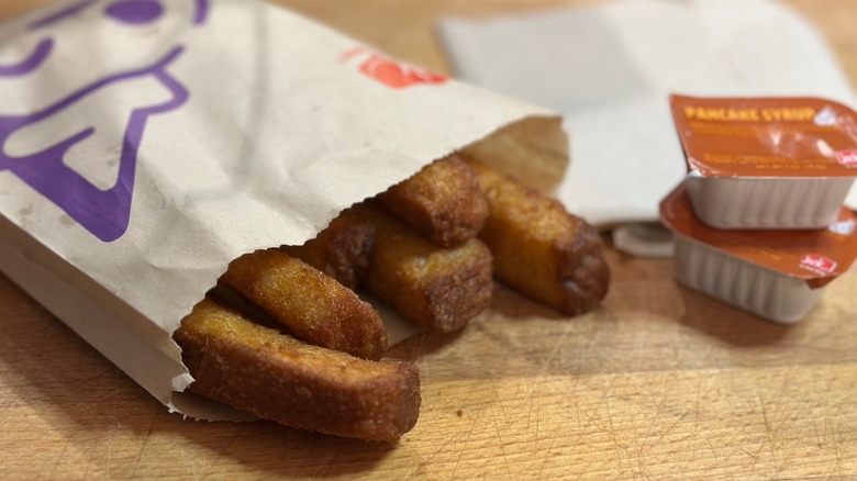 Jack in the Box French Toast Sticks in white paper bag with two packets of syrup
