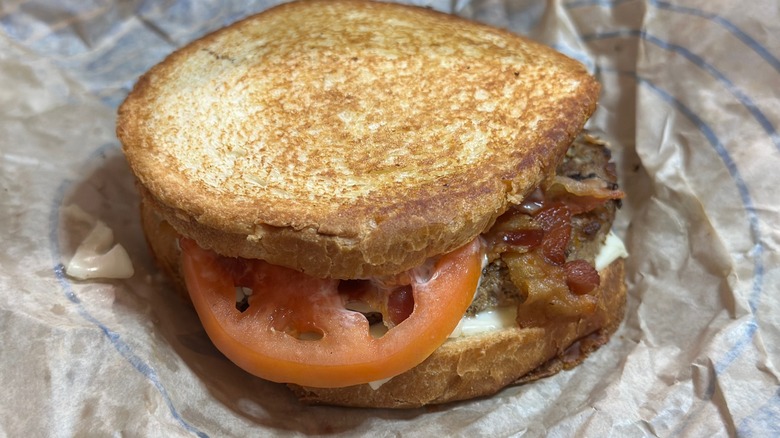 A sourdough jack from Jack in the Box with tomato and bacon on foil paper