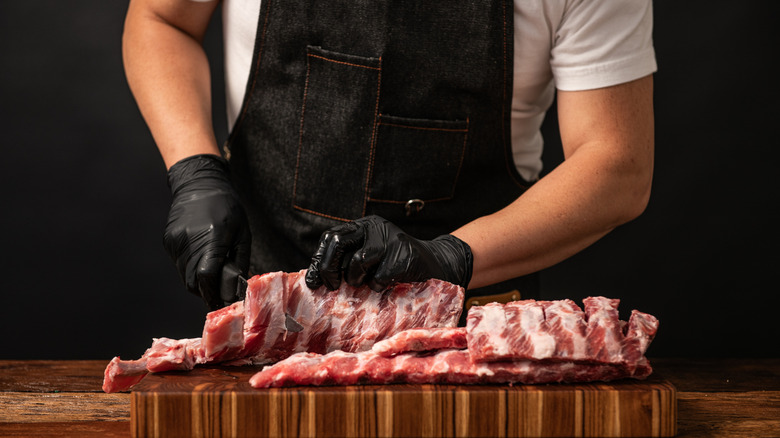 Butcher preparing raw pork ribs on a wooden cutting board