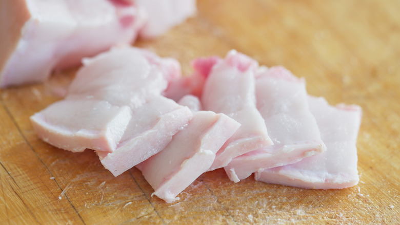 pork is turned into small pieces placed on a wooden cutting board.