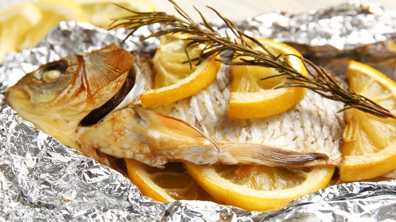 Aluminium foil with baked fish, lemon slices, and rosemary