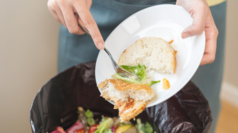 Waitress cleans food off a plate into a garbage can