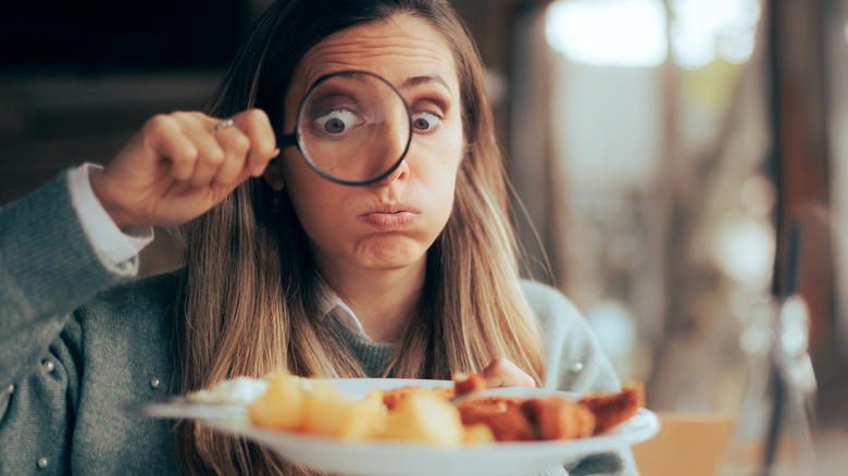 Woman uses magnifying glass to look at food at a restaurant