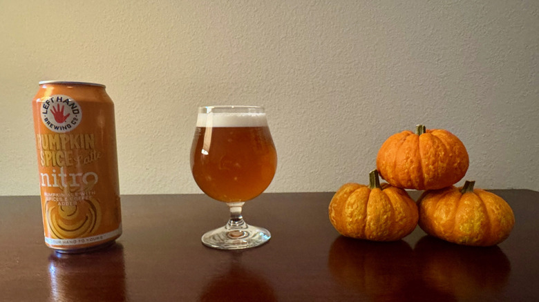 An orange can of Left Hand Brewing Company Pumpkin Spice Latte Nitro next to a glass of orange beer and three small stacked pumpkins.