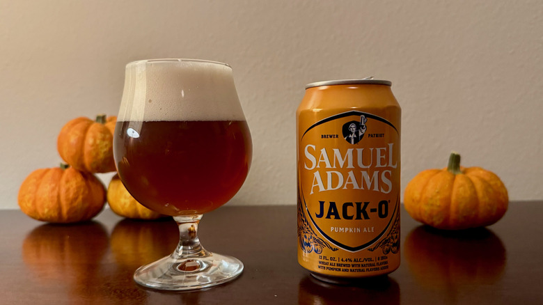 An orange can of Samuel Adams Jack-O next to a full beer glass and several small pumpkins.