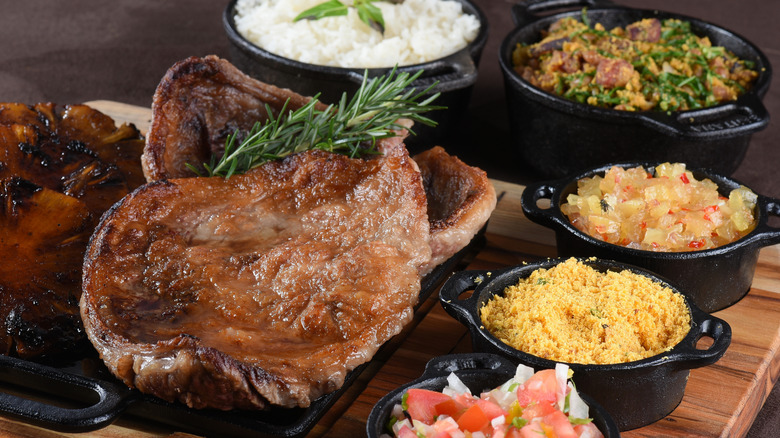 A cut of steak surrounded by Brazilian side dishes served in miniture cast iron pots on a cutting board.