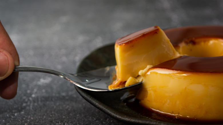 A spoon scoops a piece of Brazilian flan from where it sits on a black plate.