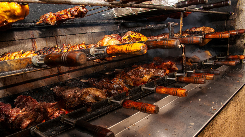 Several skewers of meat rest on a rack over an open flame.