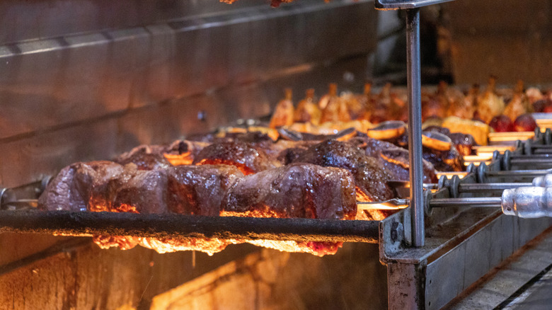 Several skewers of meat roast on an open flame at a Brazilian steakhouse.