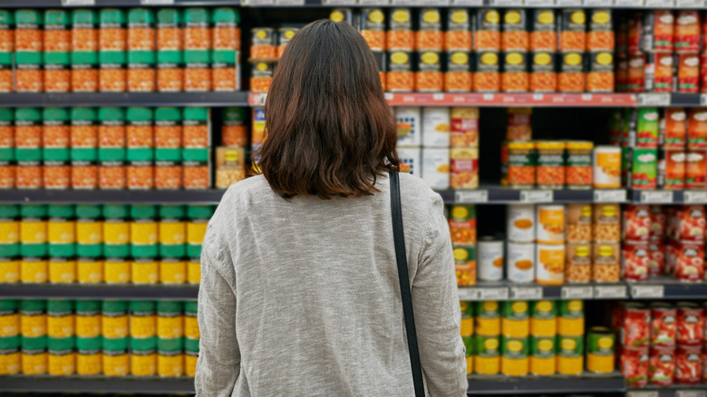 Woman standing in front of fully stocked canned food shelf at grocery store