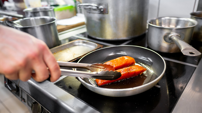 Tongs reaching toward frying pan with two fillets of salmon