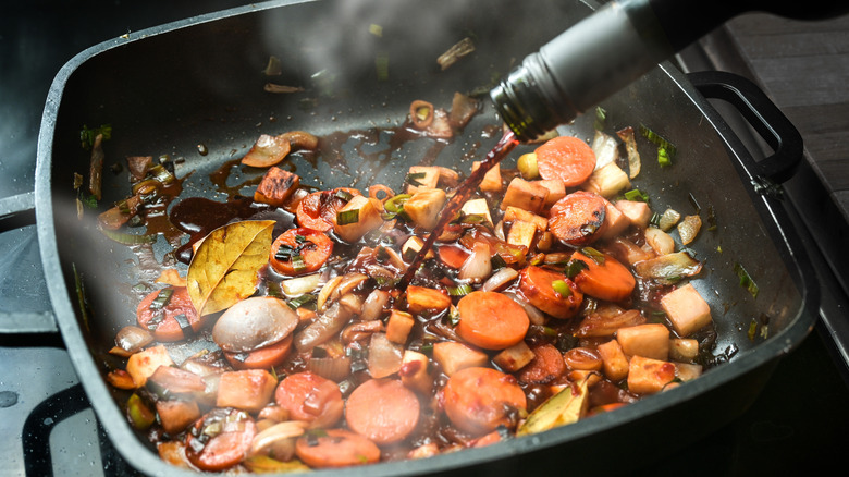Red wine being poured into a deep pan with a vegetable saute
